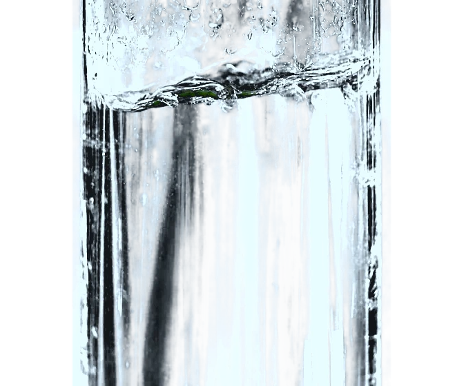 Eine Limette fällt in ein Wasserglas und Luftblasen steigen auf